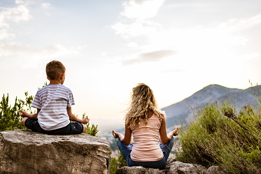 Young woman and her son preforms yoga in mountains at sunset.