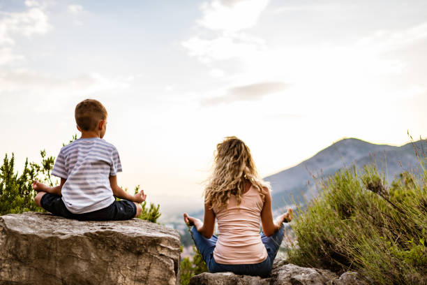 young woman and boy preforms yoga in mountains at sunset - zen like nature breathing exercise sitting imagens e fotografias de stock