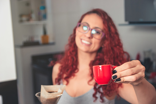 Red haired girl wearing glasses drinking a cup of coffee in her apartment