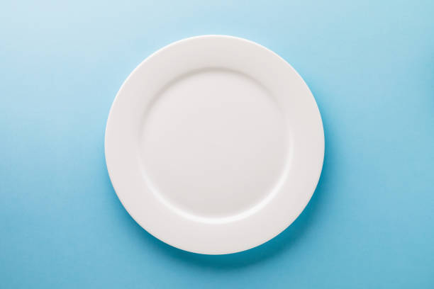 istock Flat ceramic plate white on a blue background, top view. Food background 1287843057