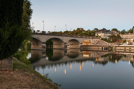 The14th-century six-span fortified stone arch bridge crossing the river Lot to the west of Cahors, in France reflected in the bright blue water of the River Lot and framed by trees