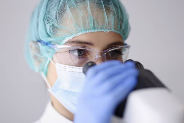 istock Woman doctor laboratory assistant in goggles and mask looks through microscope. 1287844466