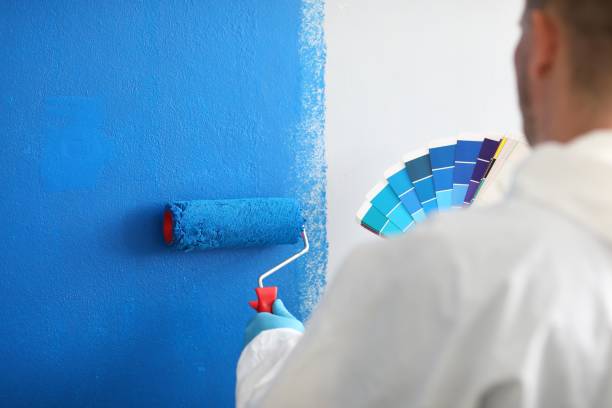 istock Craftsman holds roller and a color palette and paints white wall blue 1287846916