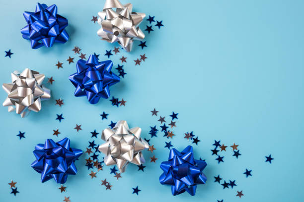 istock creative pattern with shiny bow from bright ribbon on blue background. Trendy silver,blue ribbon. Stylish metallic bows, New year 2021.Advertising flatlay,top view, copy space 1287853439
