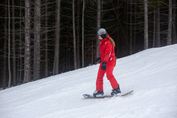 A snowboarder goes down the ski slope. A young woman goes downstairs on a snowboard. A snowboarder is riding on a gentle ski slope. The ski slope is located in a pine forest. bukovel ski resort ukraine stock pictures, royalty-free photos & images