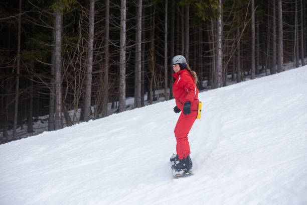 A snowboarder goes down the ski slope. A young woman goes downstairs on a snowboard. A snowboarder is riding on a gentle ski slope. The ski slope is located in a pine forest. bukovel ski resort ukraine stock pictures, royalty-free photos & images