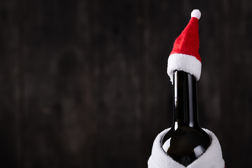 Wine bottle in Santa Claus Hat and Costume on wooden rustic background. Christmas and New Year celebration. Winter holidays