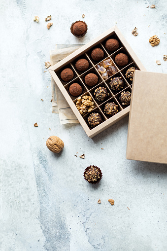 Chocolate truffle balls with cocoa powder in blank craft paper box, sweet delicious gift dessert for winter hoildays on marble background,  selective focus and copy space for text, top view