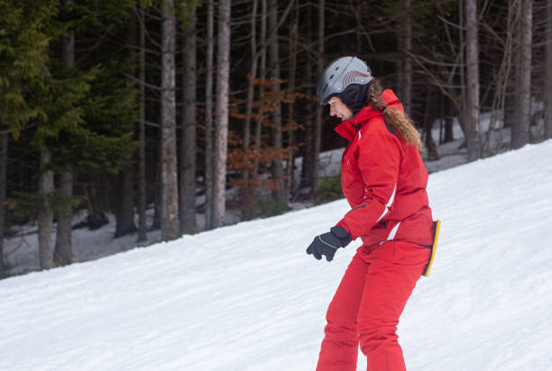 A snowboarder goes down the ski slope. A young woman goes downstairs on a snowboard. A snowboarder is riding on a gentle ski slope. The ski slope is located in a pine forest. bukovel ski resort ukraine stock pictures, royalty-free photos & images