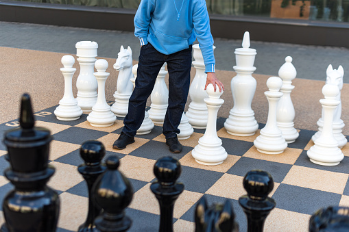 Man playing gigantic chess outdoors. Outdoor chess board with big plastic pieces. Giant size chess in public area zone. Close up big pieces and giant chess board in the park.