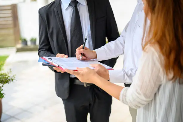 Photo of Couple signing contract agreement from real estate agent in front of their new house