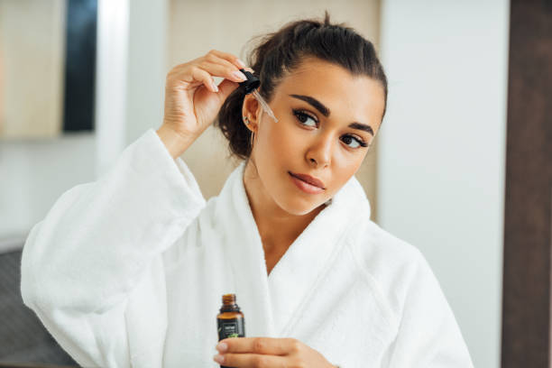 Beautiful woman using serum dropper in bathroom. Young female applying hyaluronic acid on her cheek. Beautiful woman using serum dropper in bathroom. Young female applying hyaluronic acid on her cheek. blood serum photos stock pictures, royalty-free photos & images