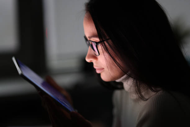 девушка в темноте смотрит на включенный экран планшета. - women dependency business time стоковые фото и изображения