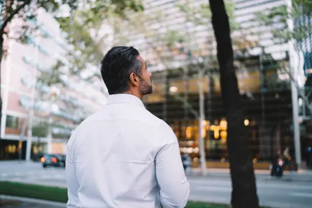 Back view of formally dressed entrepreneur thoughtful looking up in megalopolis downtown, confident corporate director thinking about business lifestyle and company building standing at urban street