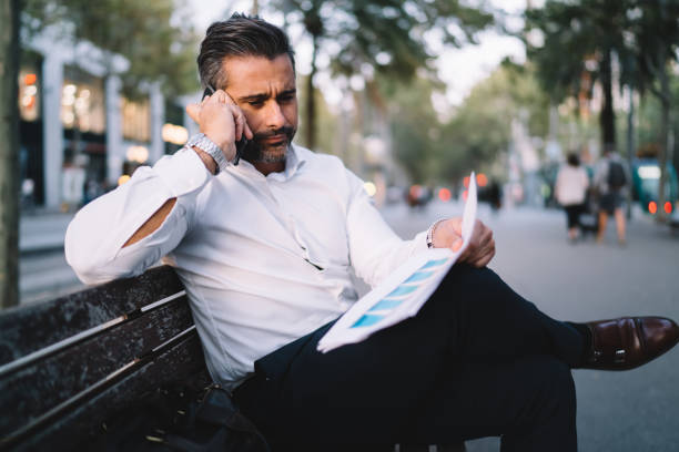 istock Middle aged professional expert calling to colleague for consultancy while analyzing paperwork and statistics, mature proud ceo connecting to 4g in roaming for making international conversation 1287863980