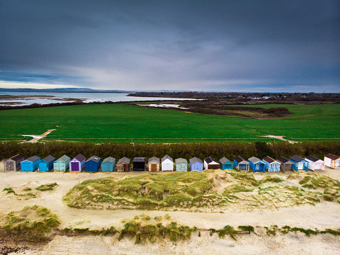 High angle shot taken by drone depicting colorful beach huts in a row on a sandy beach in Sussex, England, in winter. Room for copy space.