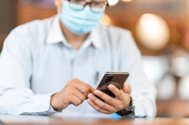 istock A businessman wearing a mask holds a phone to check e-mail 1287865897