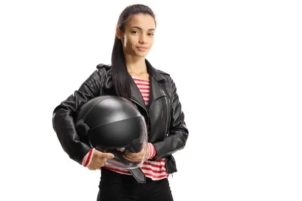 Young female biker in a leather jacket holding a helmet isolated on white background