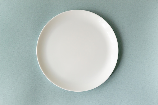 Empty white plate on a blue background. Horizontal orientation. Top view. Copy space.