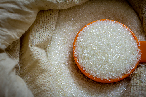 Azúcar de caña blanca granulada en un saco con una cucharada. photo