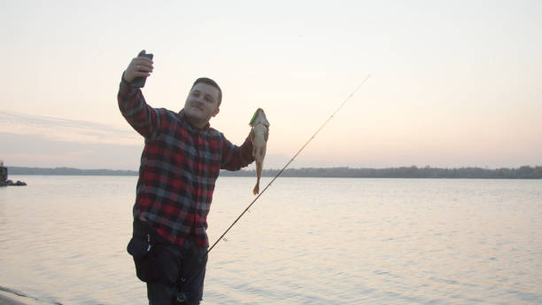 istock Male angler taking selfie with fish near water 1287873868