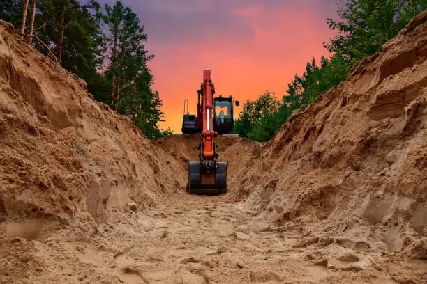 Excavator dig trench at forest area on amazing sunset background. Backgoe on earthwork for laying crude oil and natural gas pipeline or water main pipes. Construction the sewage and drainage