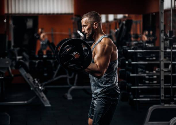 istock Handsome man doing biceps lifting barbell in a gym. Side view 1287874600