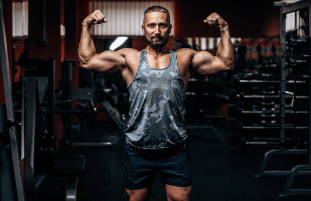 istock Man bodybuilder shows muscular body and biceps in gym 1287874601