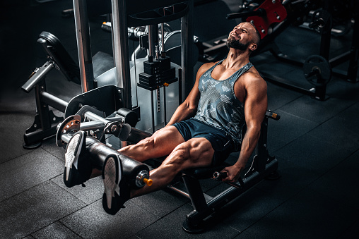 Hombre musculoso usando máquina de pesas para piernas en el gimnasio. Entrenamiento duro photo