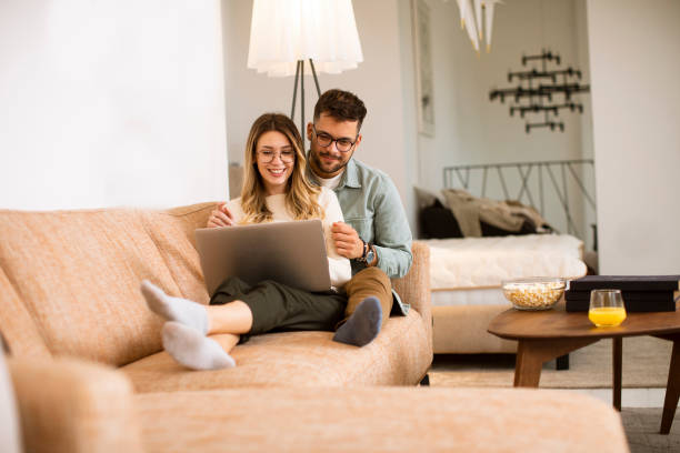 istock Young couple using laptop together while sitting on sofa at home 1287875980