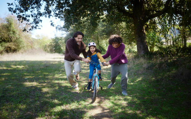 parents aidant la fille apprenant à monter un vélo à l’extérieur - roue stabilisatrice photos et images de collection