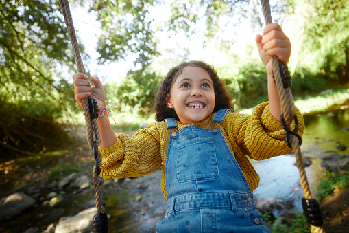 Happy small african-american girl swinging on tree wooden swing having fun in the woods by the river