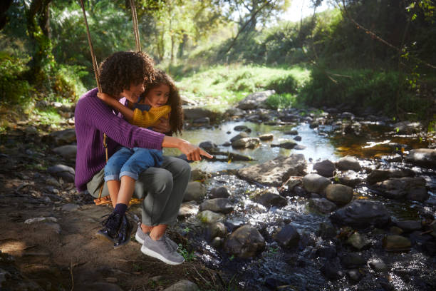 istock Mother and daughter swing in tree swing looking at river 1287883090