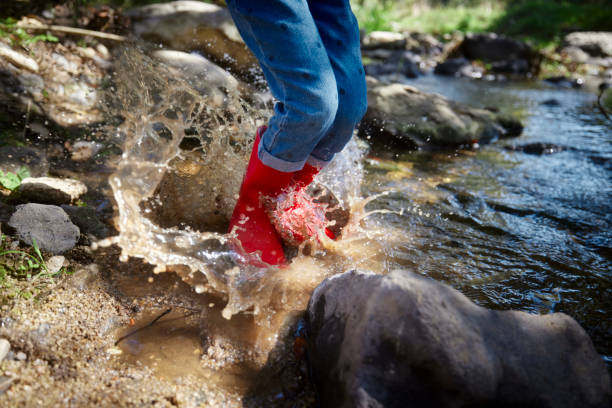 Low-section of small girl jumping on a pond with red boots