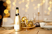 Christmas table setting with holiday decorations in a gold color. New Year celebration. A bottle and glass of champagne.