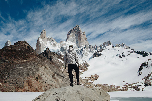 Young Caucasian man in white jacket standing on the rock and enjoy the scenic view of Mount Fitzr Roy near Laguna de los Tres in Patagonia