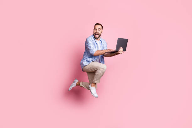 pełna długość zdjęcia podekscytowany facet uruchomić skok trzymać komputer nosić koszulę w kratę spodnie trampki izolowane różowy kolor tła - jumping people zdjęcia i obrazy z banku zdjęć