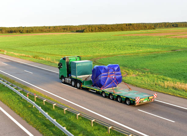 istock Truck driving along highway on blue sky background. Heavy duty tractor unit with push-pull 6x2. Logistics of transportation of heavy and oversized cargo by road 1287891242
