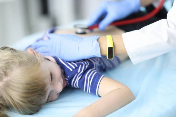 고무 장갑을 낀 소아과 의사가 클리닉 초상화에서 소파에 누워있는 아이의 폐를 듣습니다. - 세기관지 뉴스 사진 이미지