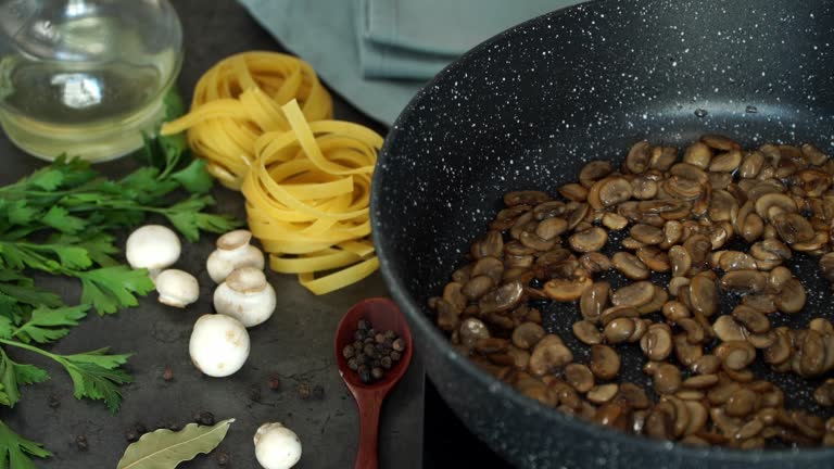 Close up of champignons is fried in pan on stove on background of pasta, mushrooms and greens. Italian Cuisine