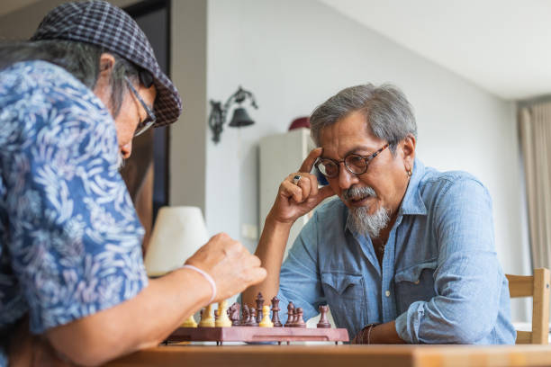 アジアの先輩男性の友人は自宅でリビングルームでチェスをしている、アクティブな高齢者のコンセプト - chess mate ストックフォトと画像