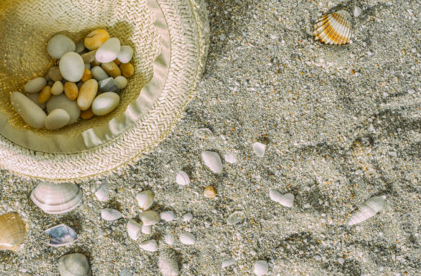 istock Pebbles in a hat on a sandy beach, top view with copy space. Summer vacation and travel concept. 1287910416