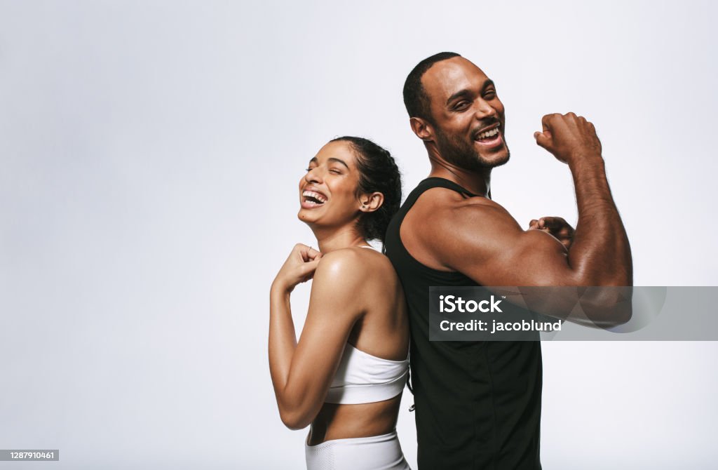 Cheerful fit couple on white background Smiling fitness couple standing back to back against white background. Fit couple showing arm muscles standing together. Exercising Stock Photo