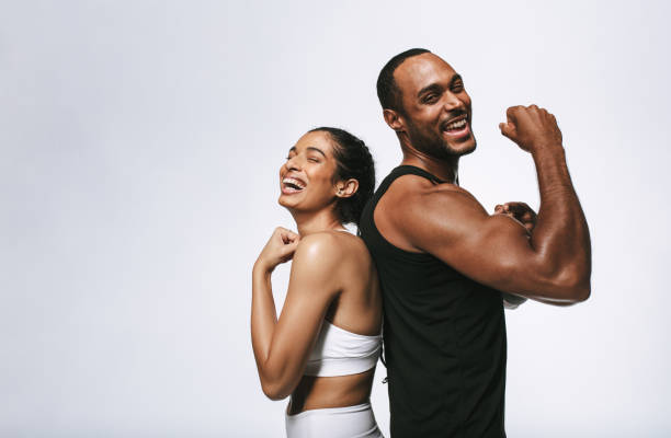 Cheerful fit couple on white background Smiling fitness couple standing back to back against white background. Fit couple showing arm muscles standing together. body building photos stock pictures, royalty-free photos & images
