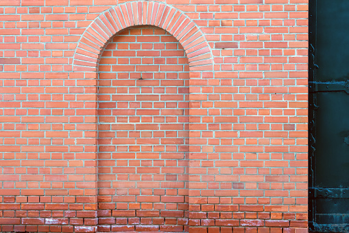 Decorative pseudo door in the red brick wall next to the black forged gate