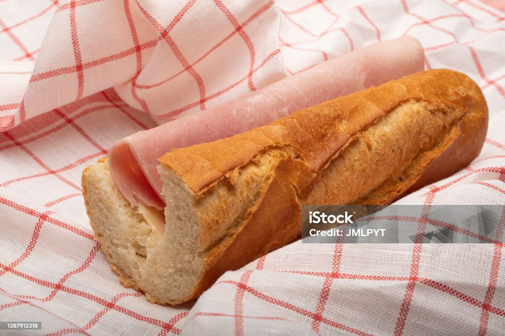 ham sandwich with a French baguette ham and butter sandwich with a red and white checkered tea towel in the background, close up. Ham Stock Photo