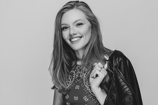 happy casual girl holding leather jacket over shoulder, smiling and posing on black and white background in studio