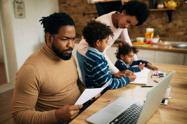 istock Black father working on laptop while mother is homeschooling their kids. 1287923414