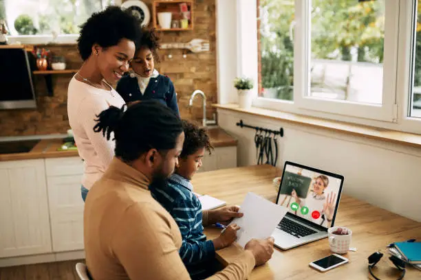 Photo of Happy African American woman reminding her husband to finish with work on laptop so that kids could follow online classes at home.