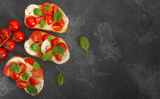 Caprese bruschetta toasts with mozzarella, cherry tomatoes and fresh garden basil.Traditional italian appetizer or snack, antipasto. Top view with copy space. Flat lay